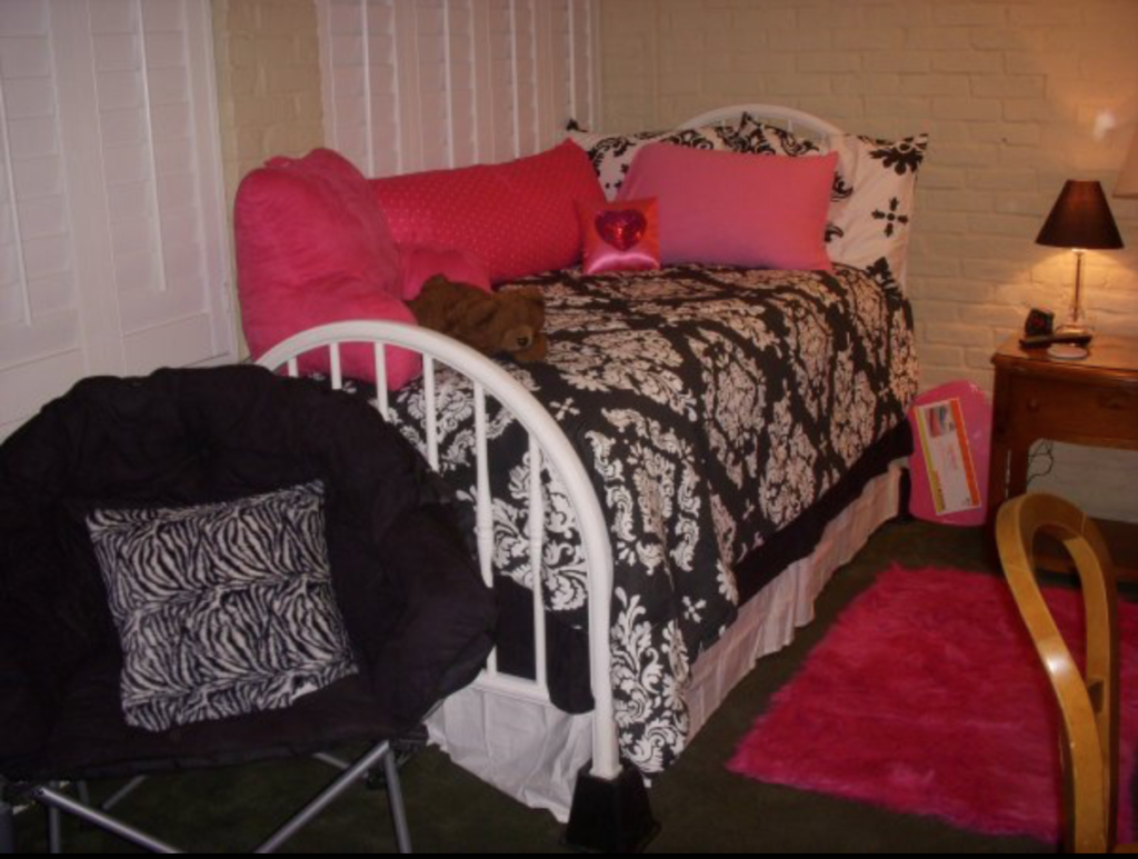 black and white bedding with white bed frame, pink rug, black char, pink throw pillows, exposed brick wall