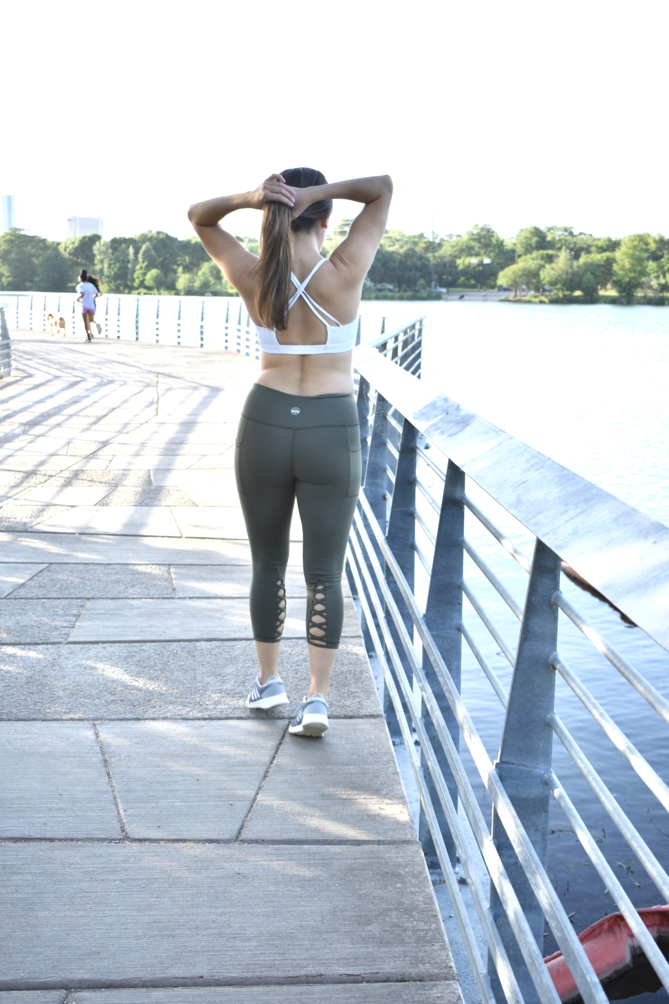 hunter green workout leggings with criss cross details, white sports bra and grey adidas running shoes